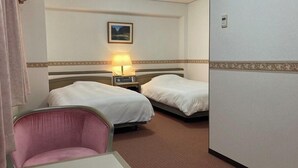 Hotellihuone, jossa on kaksi sänkyä, tuoli, yöpöytä lampun kanssa ja taulu seinällä.
