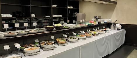 Montaje de bufé con diversos platos y recipientes, incluyendo fuentes y bandejas, dispuesto sobre una mesa larga con mantel blanco.