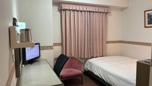 Hotellihuone, jossa on sänky, työpöytä tietokoneella, tuoli ja ikkuna, jossa on verhot.