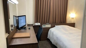 Habitación de hotel con escritorio, computadora, teléfono, cama y luz empotrada en la pared.