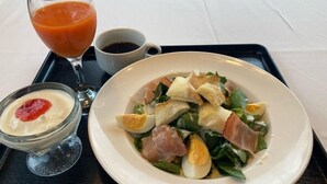 Un plato con ensalada de huevos, jamón y vegetales verdes, acompañado de un vaso de jugo de naranja y una taza de café.
