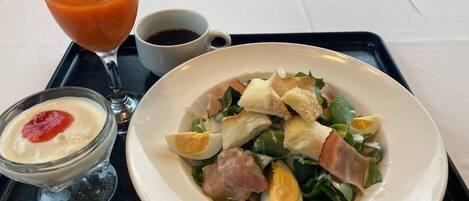 Een maaltijd bestaande uit een salade met eieren, ham en groenten, vergezeld van een glas sinaasappelsap en een kop koffie.