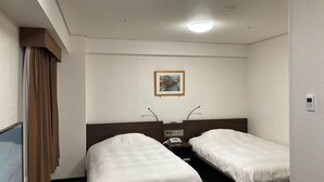 Una habitación de hotel con dos camas individuales, una mesita de noche con teléfono, un cuadro en la pared y una ventana con cortinas.