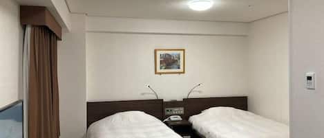 A hotel room with two single beds, a bedside table with a phone, a painting on the wall, and a window with curtains.