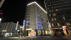 Een meerlaags hotel met verlichte signage, een voetgangersoversteek en aangrenzende gebouwen.