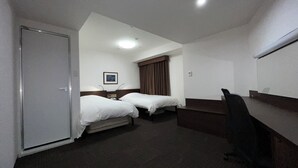 Een hotelkamer met twee eenpersoonsbedden, een bureau, een stoel, een kledingkast en een plafondlamp.
