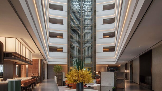 Hall moderna di un hotel con un atrio centrale, zone relax e un bar.