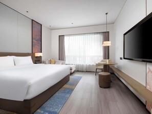 Une chambre d’hôtel moderne dotée d’un grand lit, d’un bureau, d’une télévision et d’une grande fenêtre avec des rideaux.