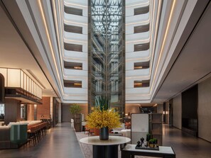 A modern hotel lobby with a central atrium, seating areas, and a bar.