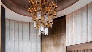 Una hall moderna con un originale lampadario geometrico, un tavolo rotondo centrale con un vaso di fiori gialli e una reception in marmo.