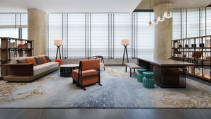 Zona relax moderna con divano, poltrone, tavolino e tavolo da pranzo. Sono presenti scaffali e un'ampia finestra che permette l'ingresso di luce naturale.