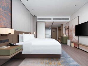Habitación de hotel moderna con una cama grande, mesita de noche, lámpara y un televisor de pantalla plana.