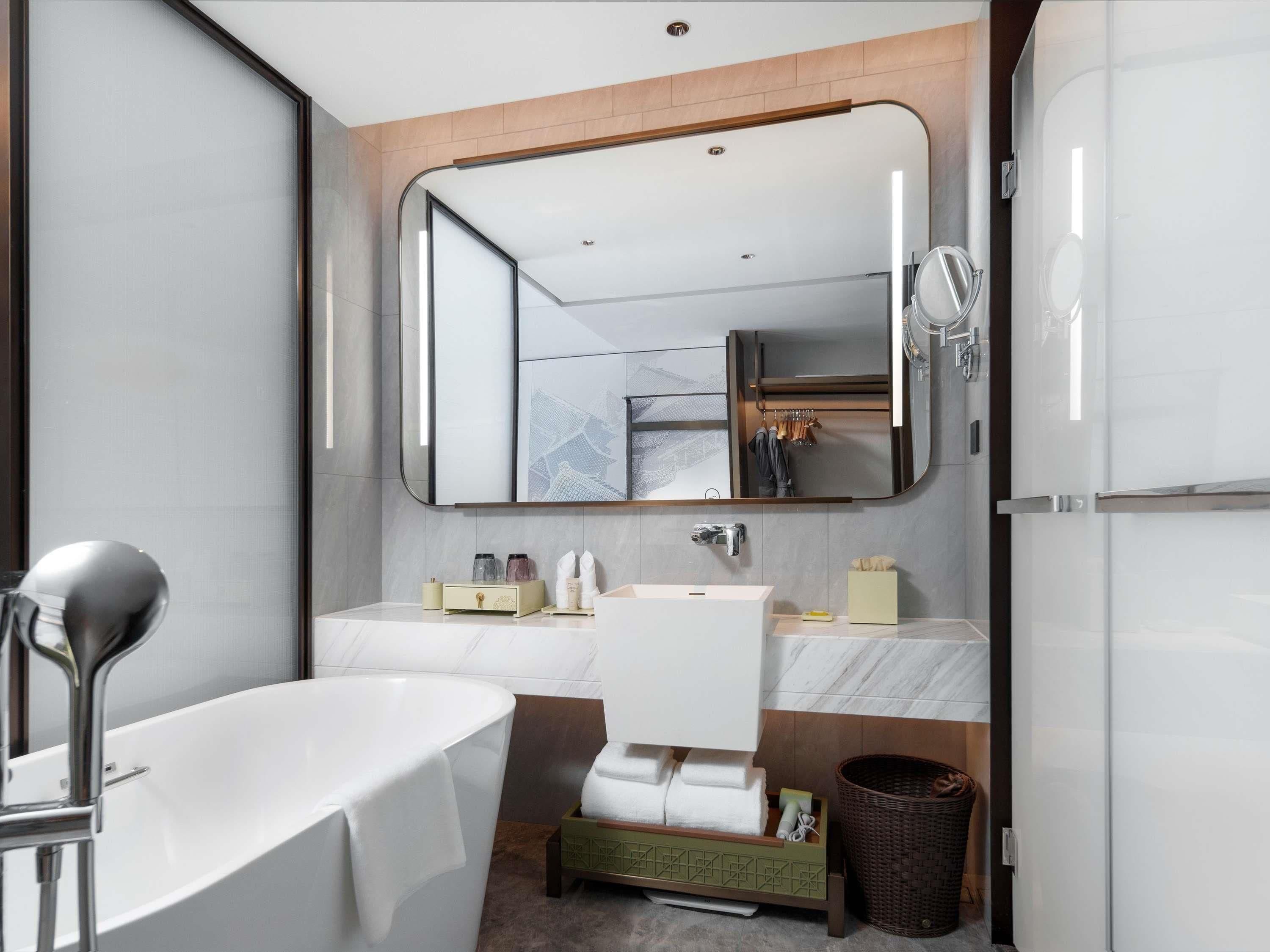 A modern bathroom with a bathtub, a large mirror, a vanity with a sink, and a shower area.