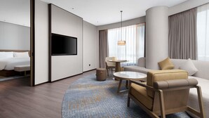 Una habitación de hotel moderna con cama, televisión, sofá, sillón y una mesita.