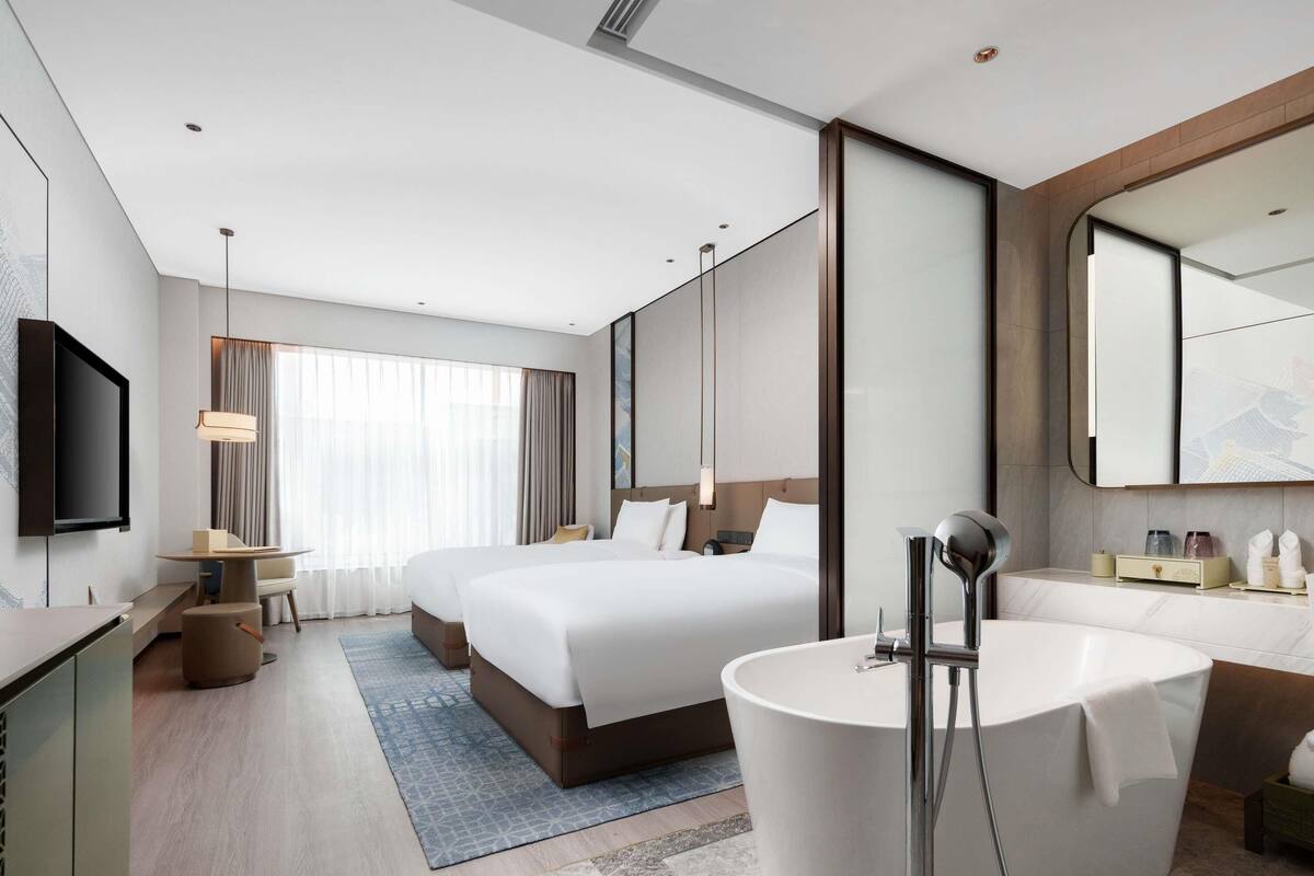 Een moderne hotelkamer met een groot bed, een aparte zithoek, een badkuip en een flatscreen-televisie.