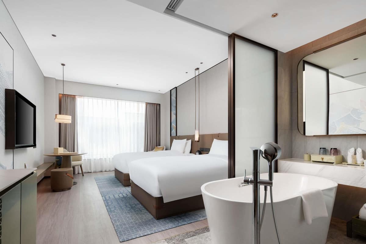 A modern hotel room with a large bed, a separate sitting area, a bathtub, and a flat-screen TV.