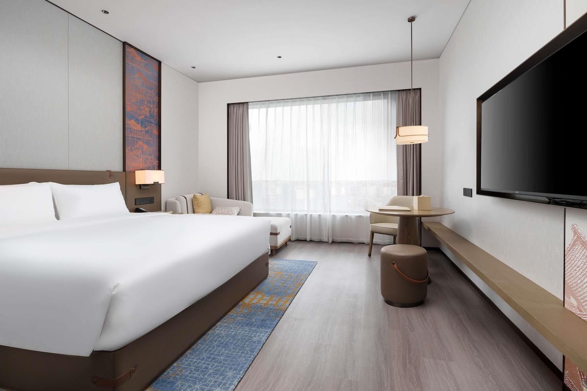 Een moderne hotelkamer met een groot bed, een bureau, een televisie en een groot raam met gordijnen.