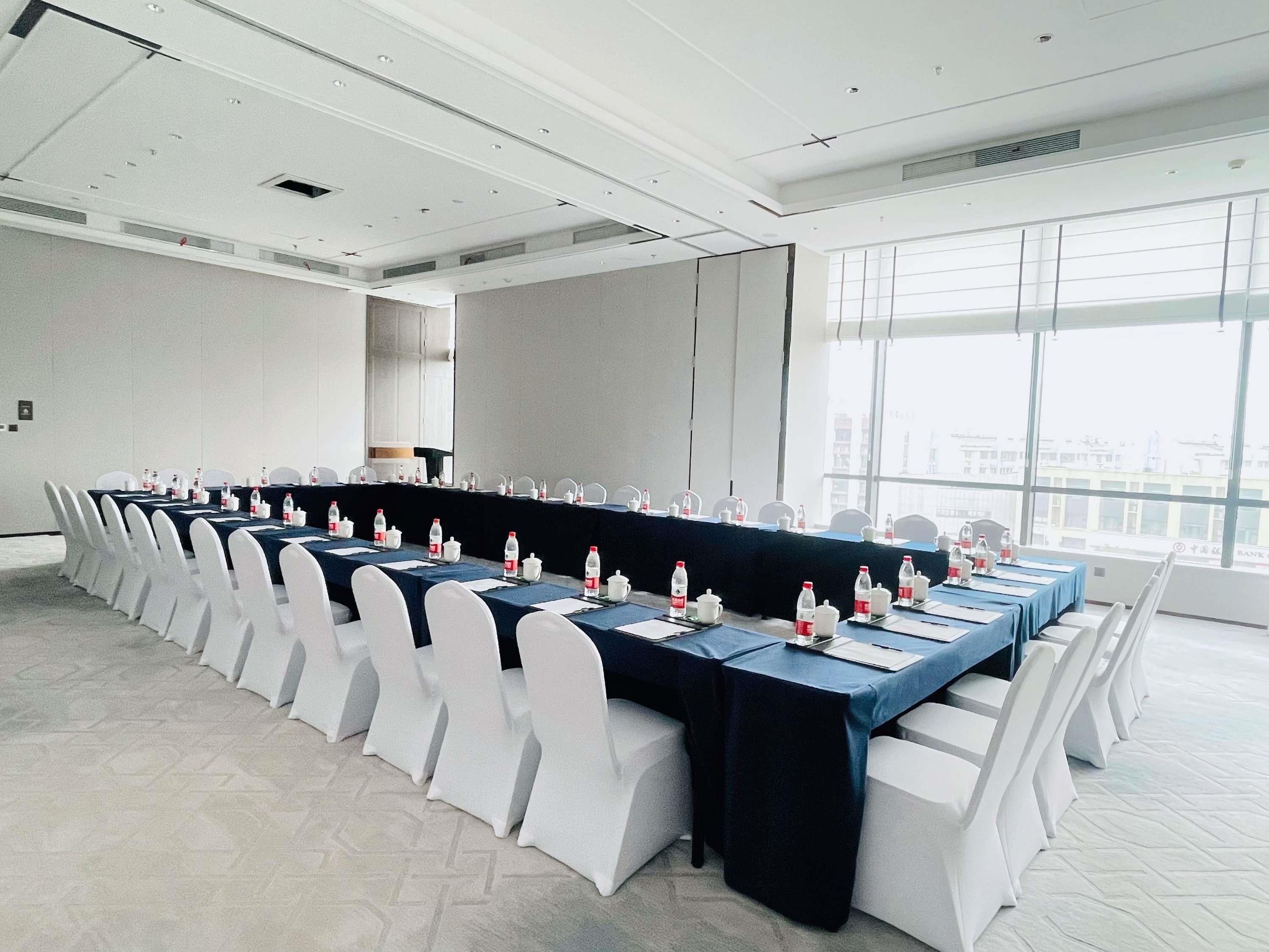 Une salle de conférence avec une longue table, des chaises blanches et des bouteilles d’eau.