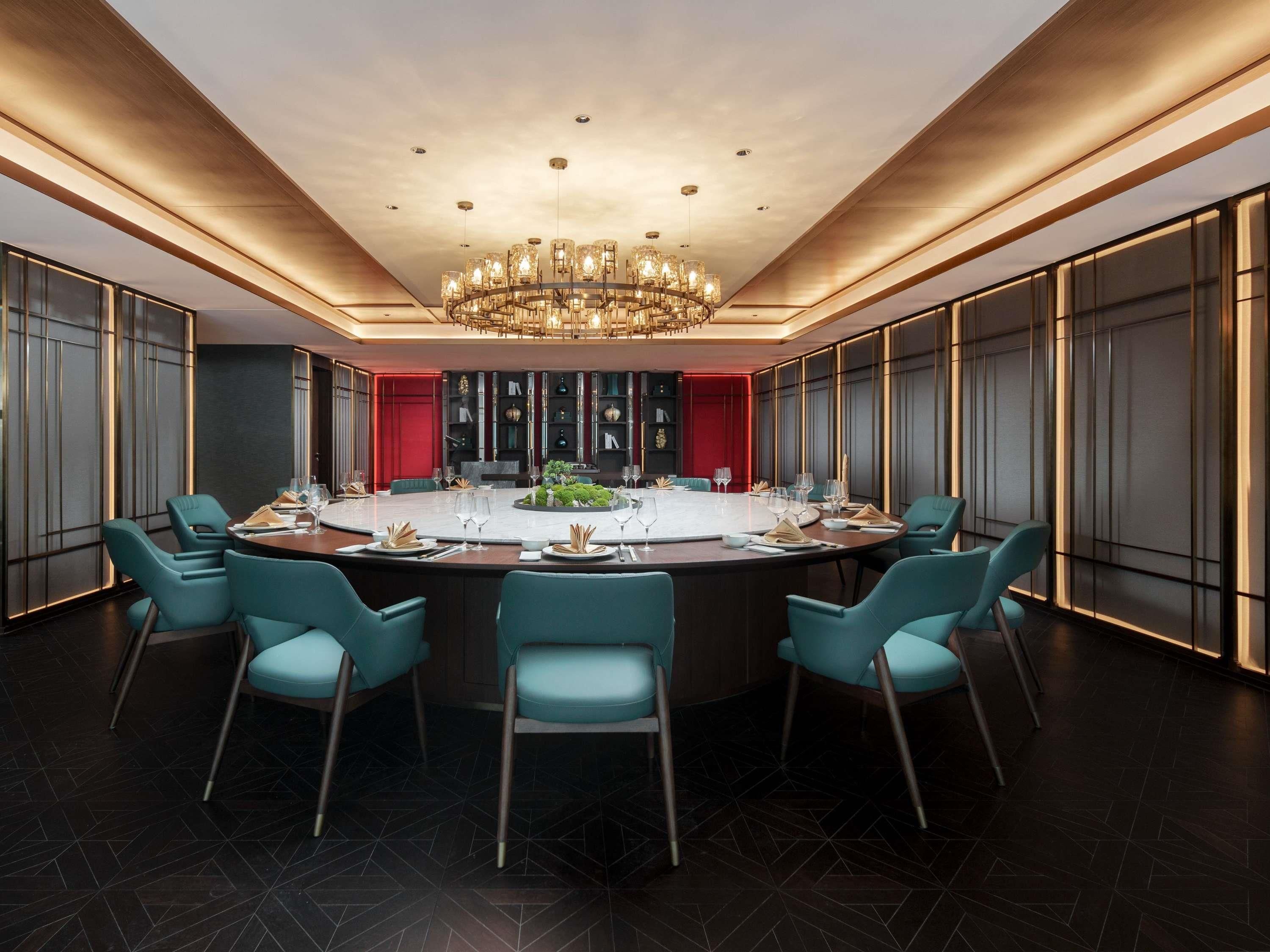 Uma sala de jantar moderna com uma mesa redonda, cadeiras cor turquesa e um candelabro.