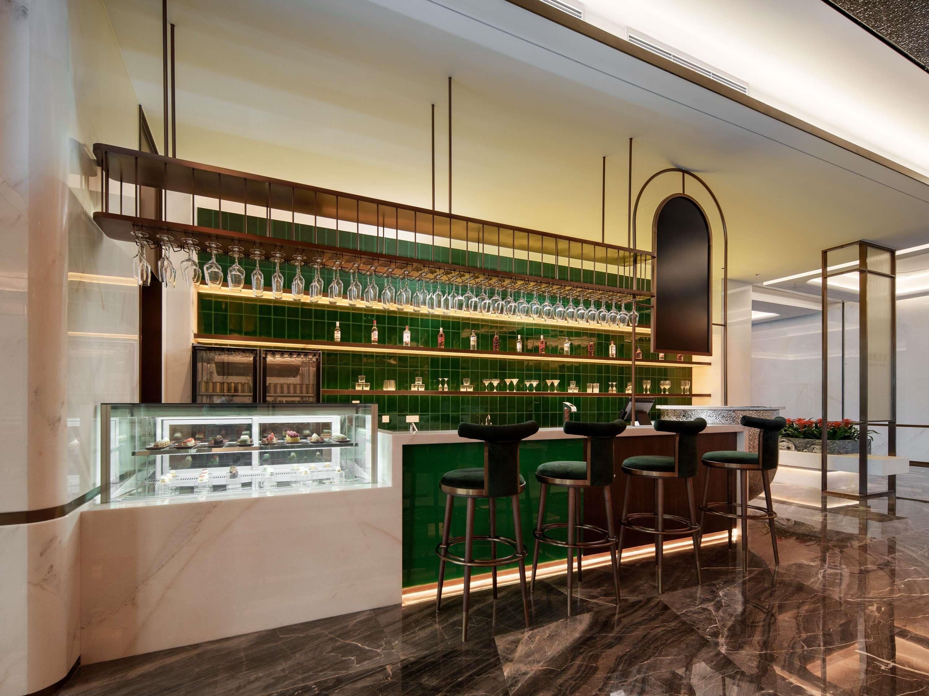 A bar area with a green tiled wall, a glass display case, and bar stools.