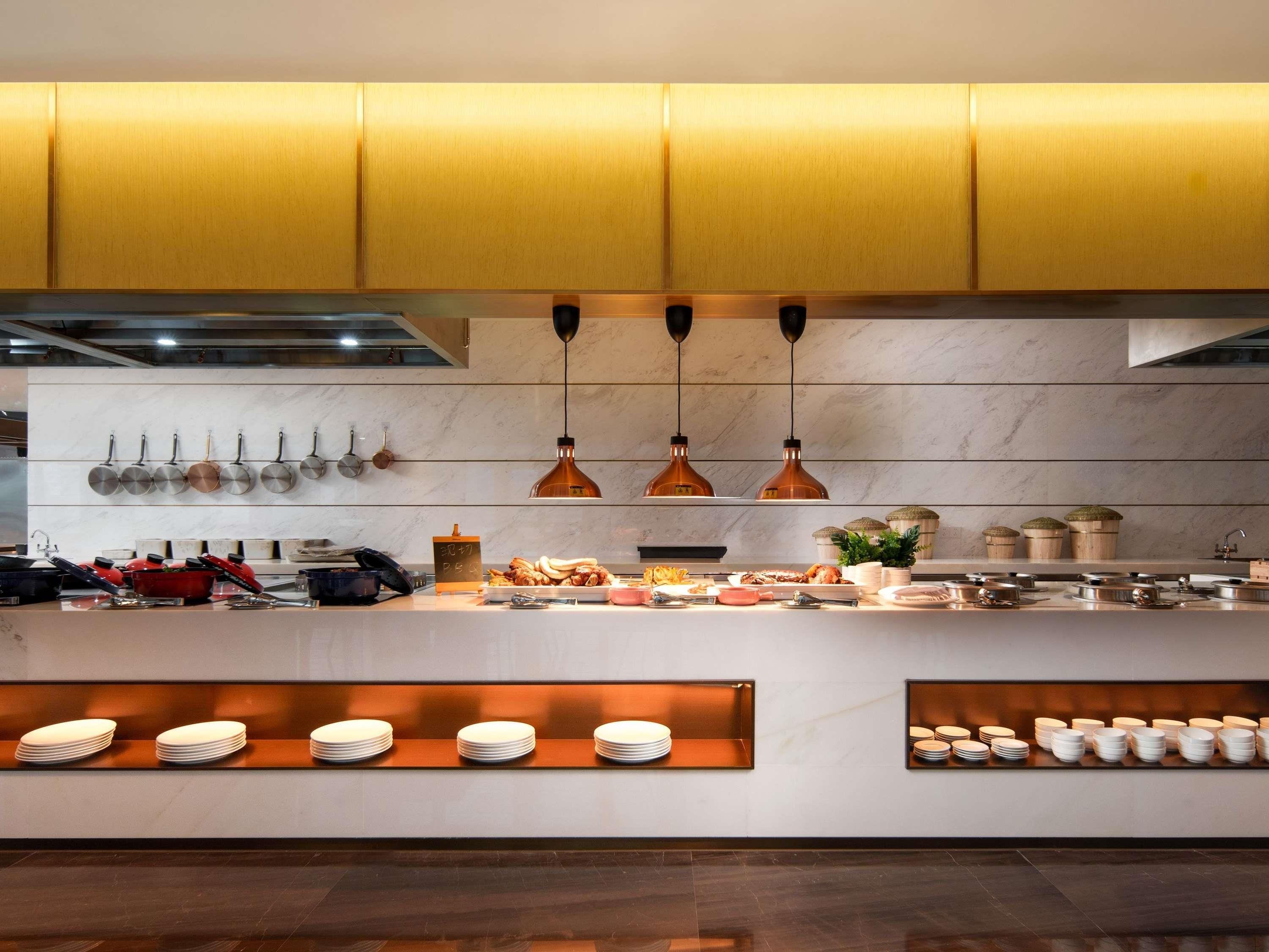 A modern kitchen with yellow cabinets, hanging pots, and a central island with plates and food items.