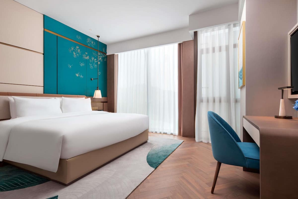 Une chambre d’hôtel moderne avec un grand lit, un bureau, une chaise et une grande fenêtre avec des rideaux.