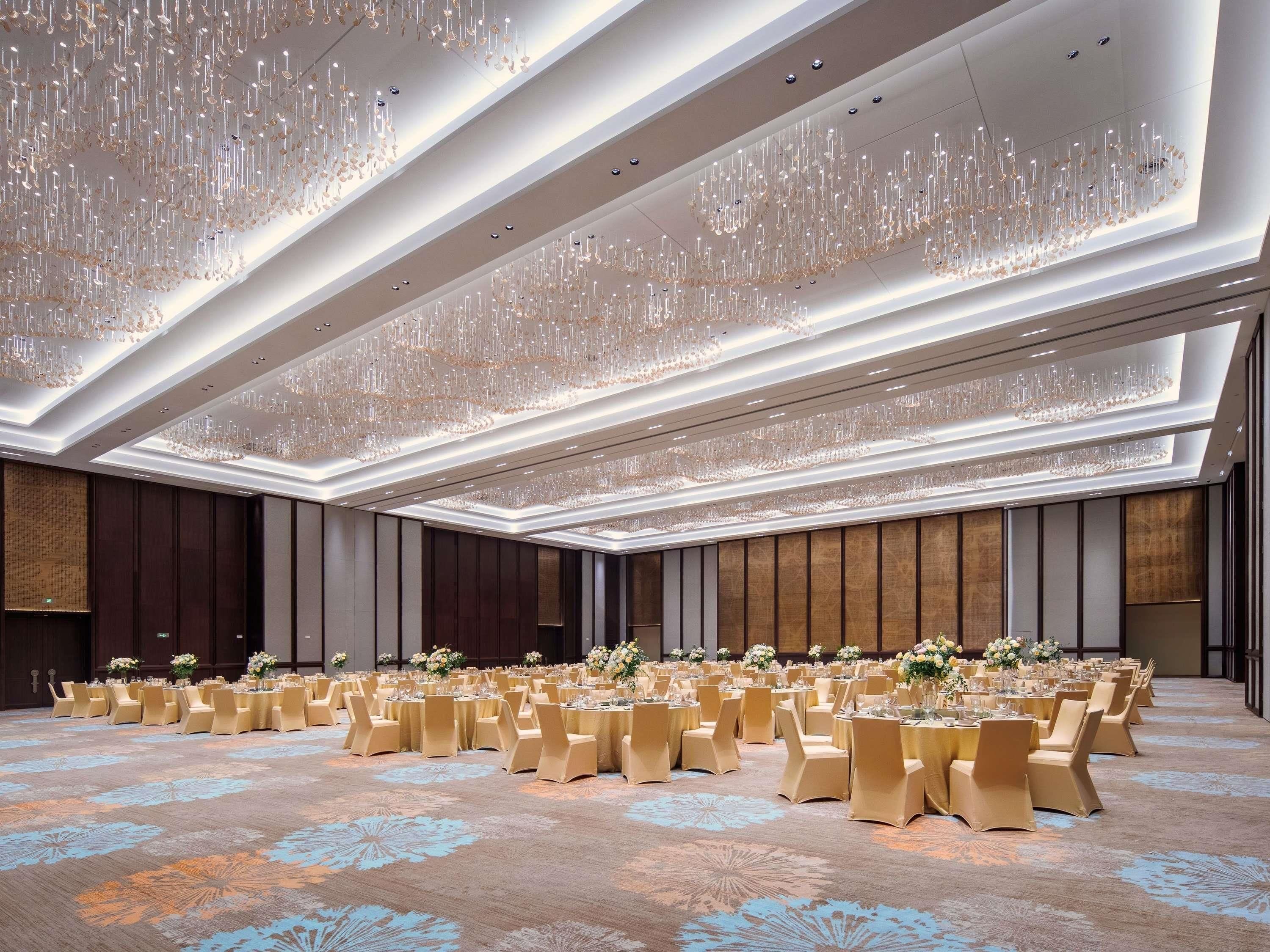 Un amplio salón de banquetes con filas de mesas redondas, cada una dispuesta con sillas y centros de mesa.