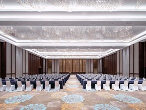 A conference room with rows of tables and chairs, a patterned carpet, and a ceiling with hanging chandeliers.