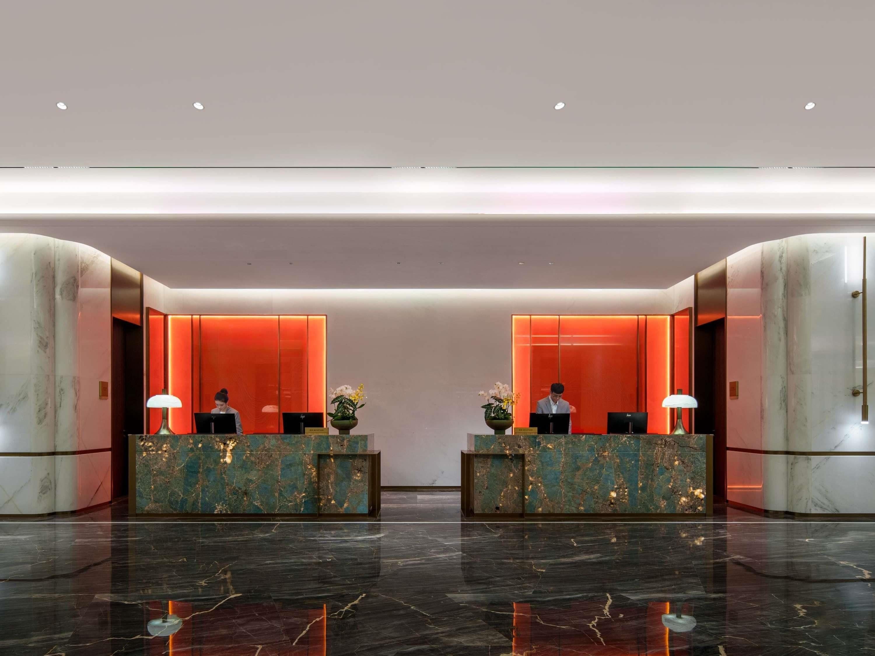 Eine moderne Hotelhalle mit Marmor-Rezeptionstheken, einer zentralen, rot beleuchteten Wand und einem polierten Marmorboden.