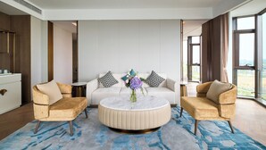A modern living room with a round coffee table, two armchairs, a sofa, and a view of the outdoors.