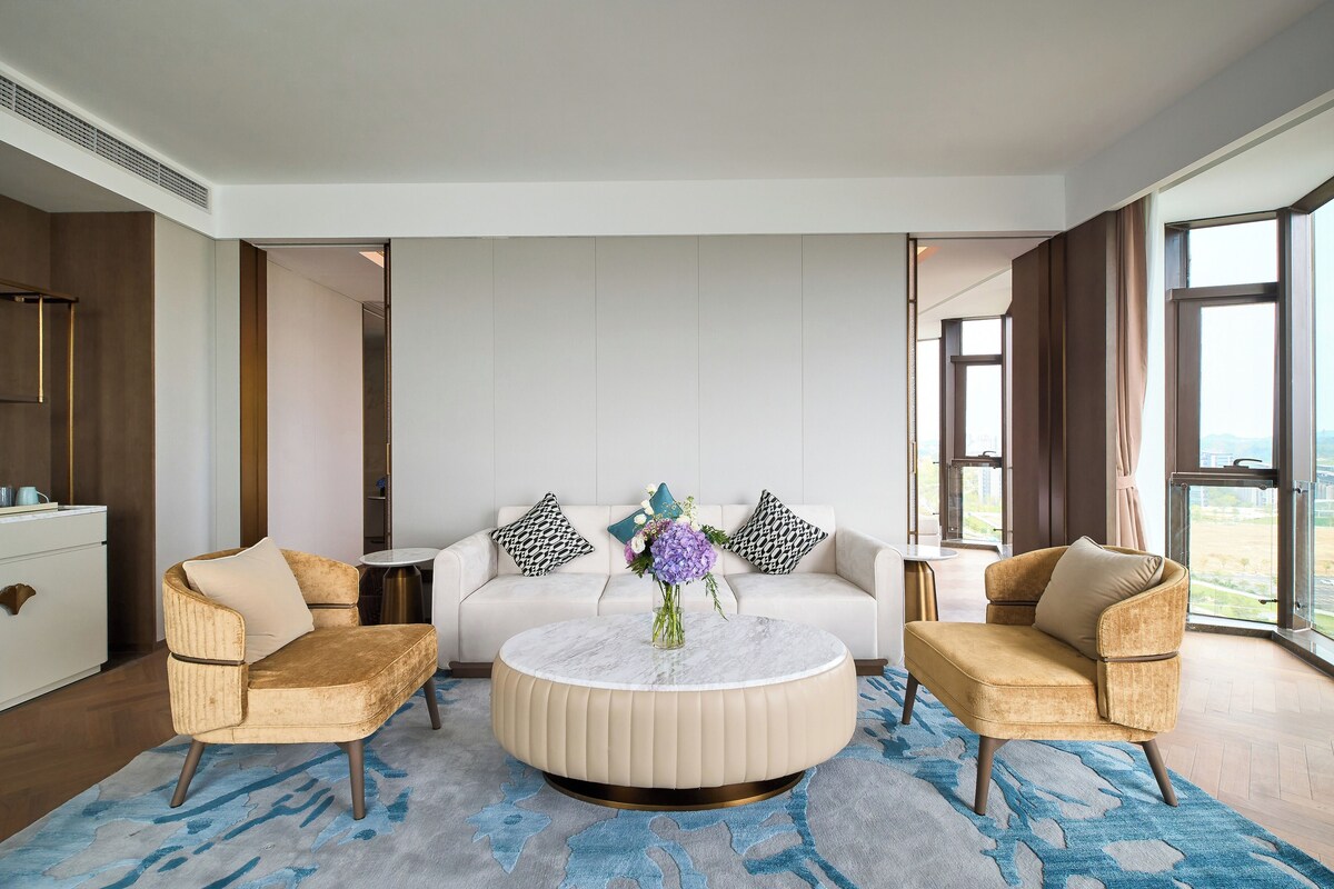A modern living room with a round coffee table, two armchairs, a sofa, and a view of the outdoors.