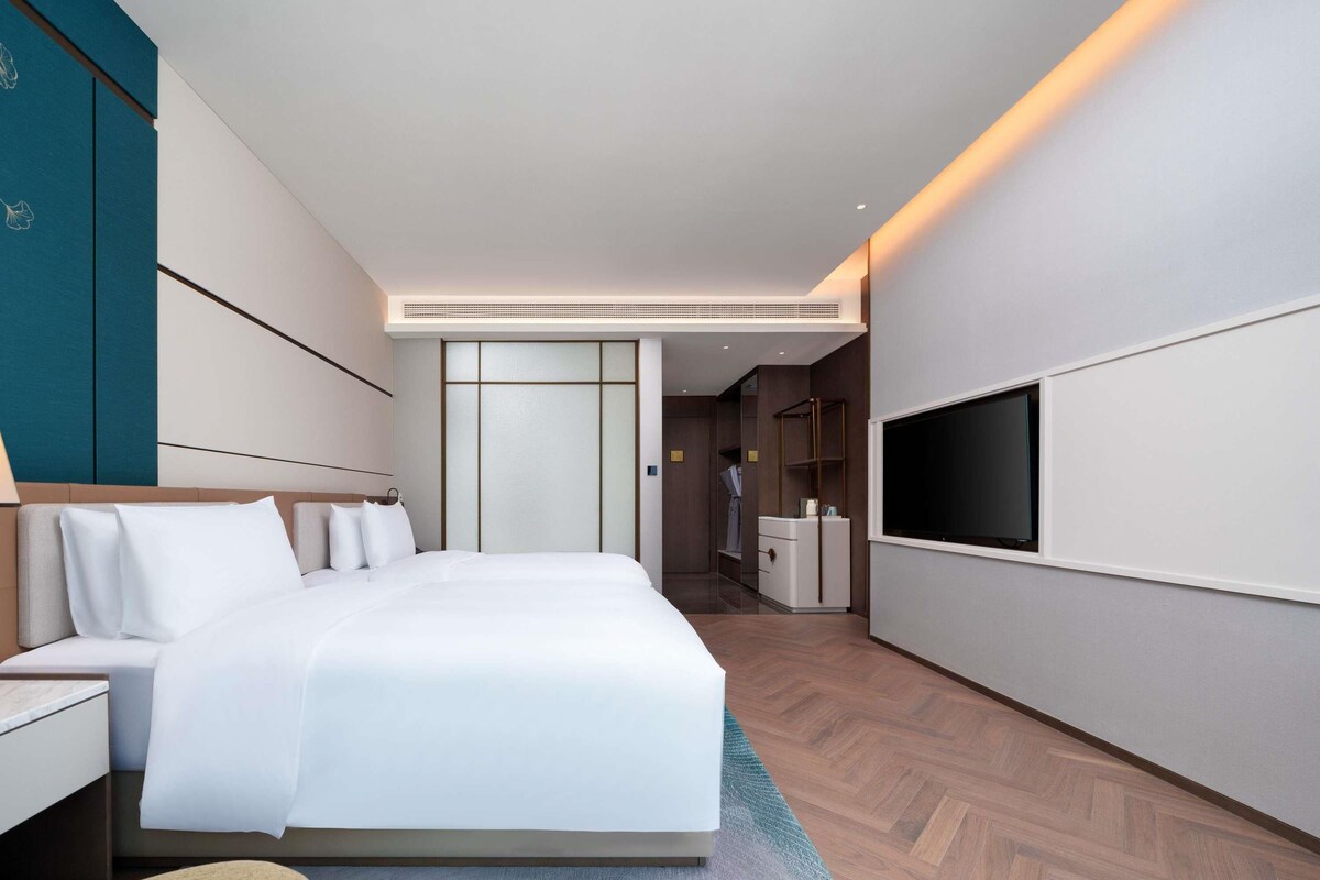 Una habitación de hotel moderna con una cama grande, un televisor montado en la pared y un vestidor.
