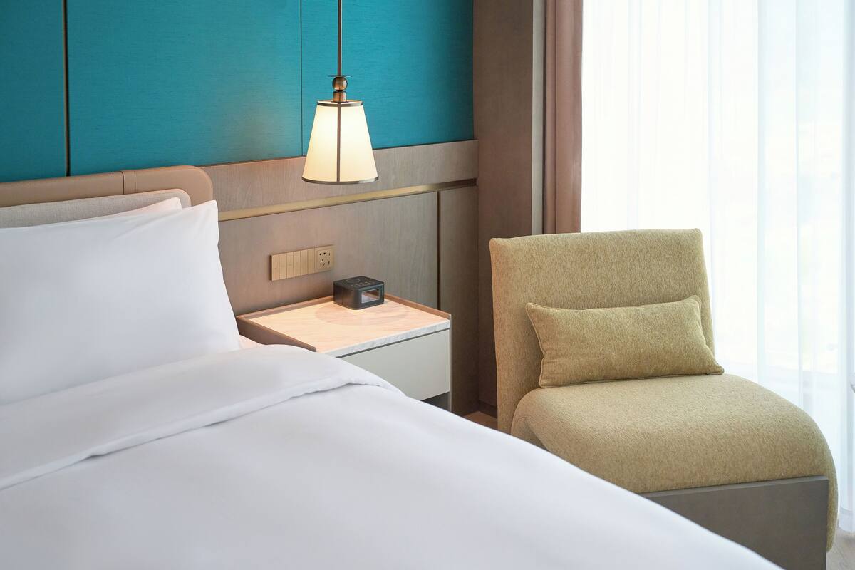 Una habitación de hotel con cama, mesita de noche, lámpara y una silla.