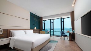 A modern hotel room with a large bed, a desk, and a chair. The room has large windows offering a view of the outdoors. - Grand Mercure Hangzhou Qingshan Lake (Hangzhou)