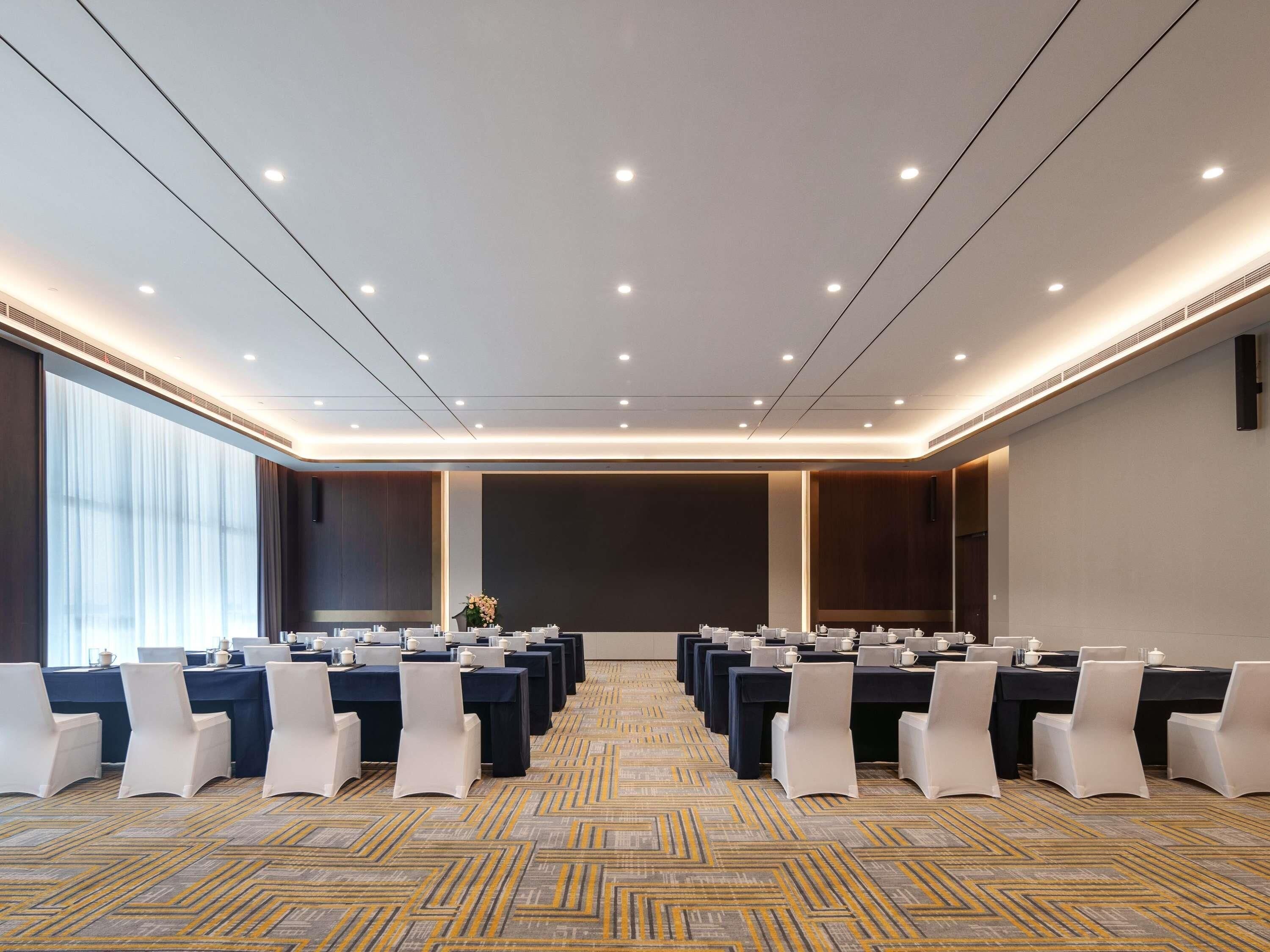 A conference room with multiple tables and chairs, a patterned carpet, and a large window with curtains.