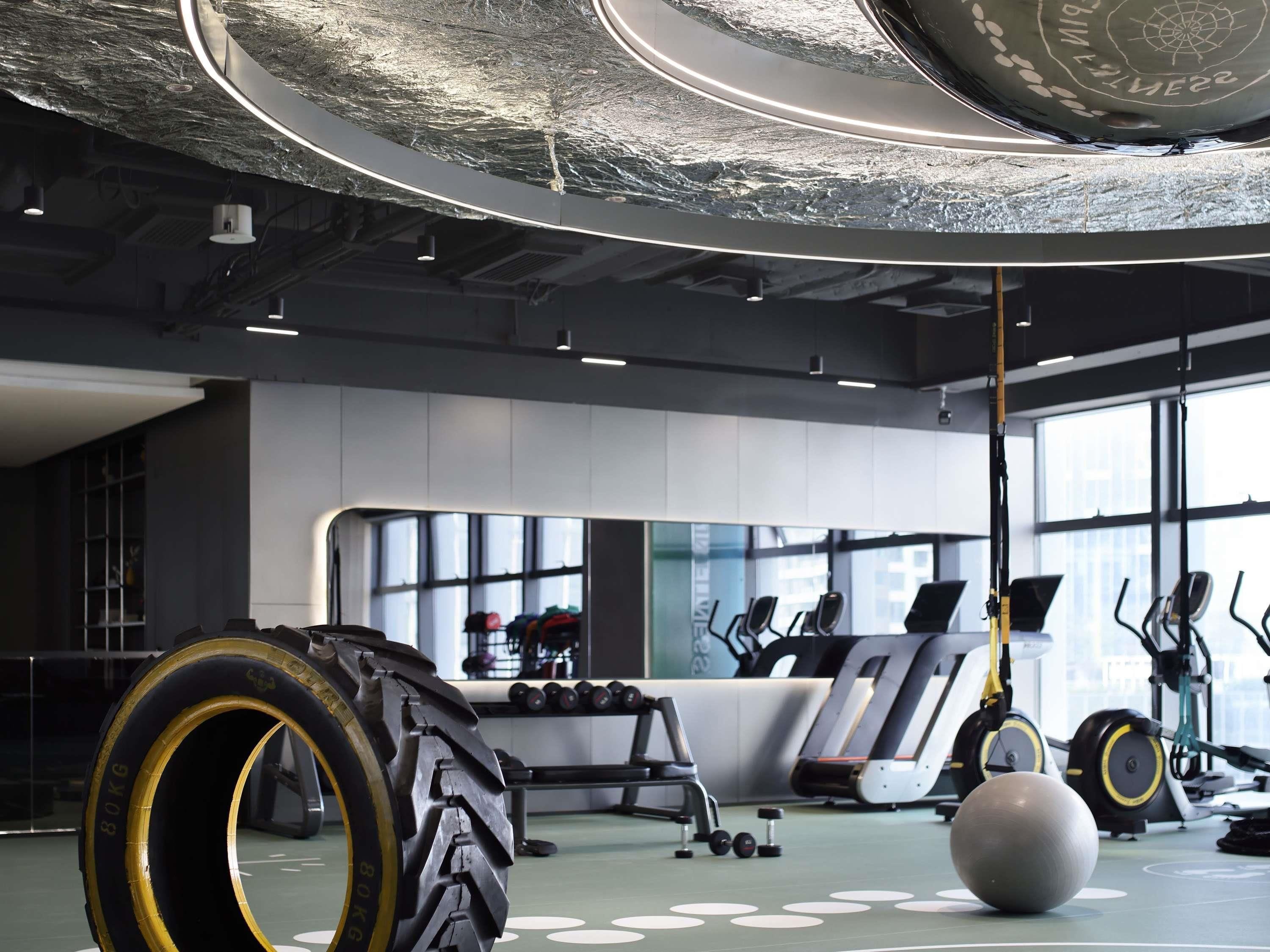 A gym with exercise equipment, large windows, and a ceiling with a circular design.