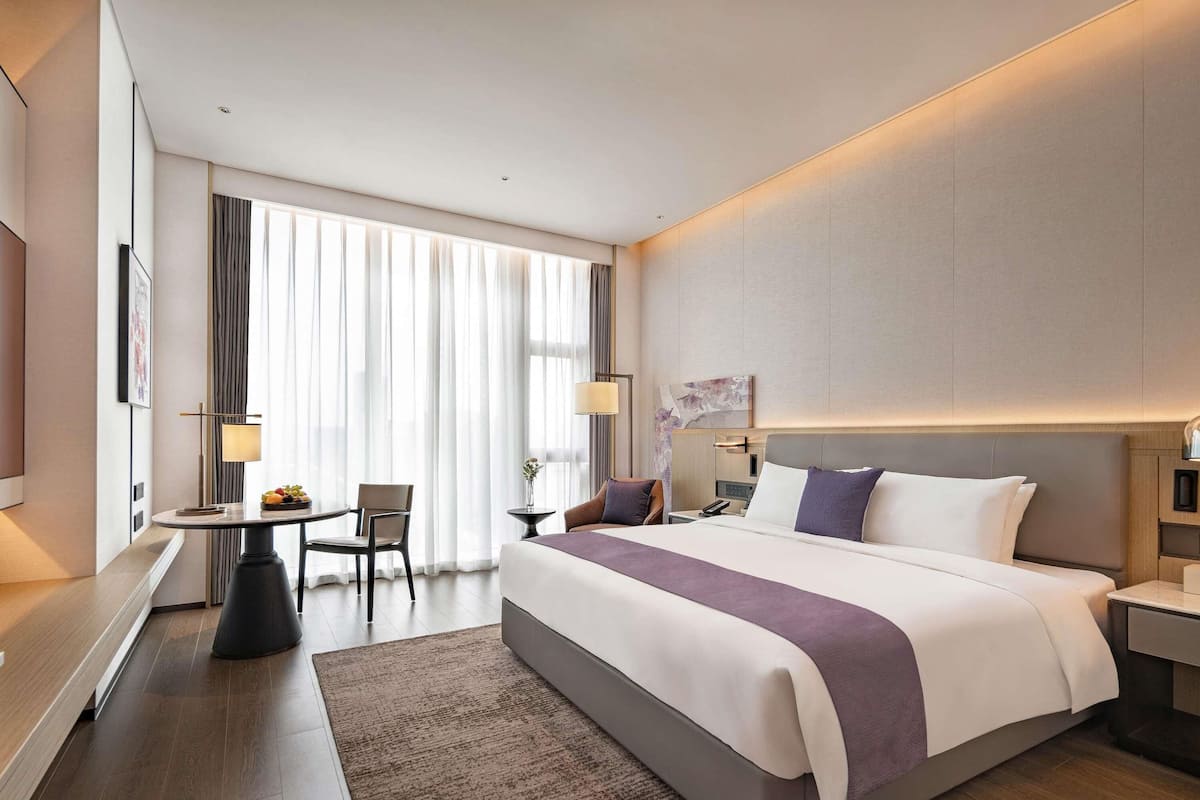 A modern hotel room with a large bed, a desk, and a chair.