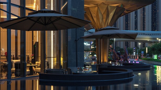 A modern outdoor seating area with umbrellas, a glass wall, and a view of the cityscape. - Grand Mercure Shenzhen Guangming (Shenzhen)