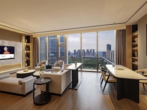 A modern living room with a TV, seating, a dining area, and a large window with a city view. - Grand Mercure Shenzhen Guangming (Shenzhen)