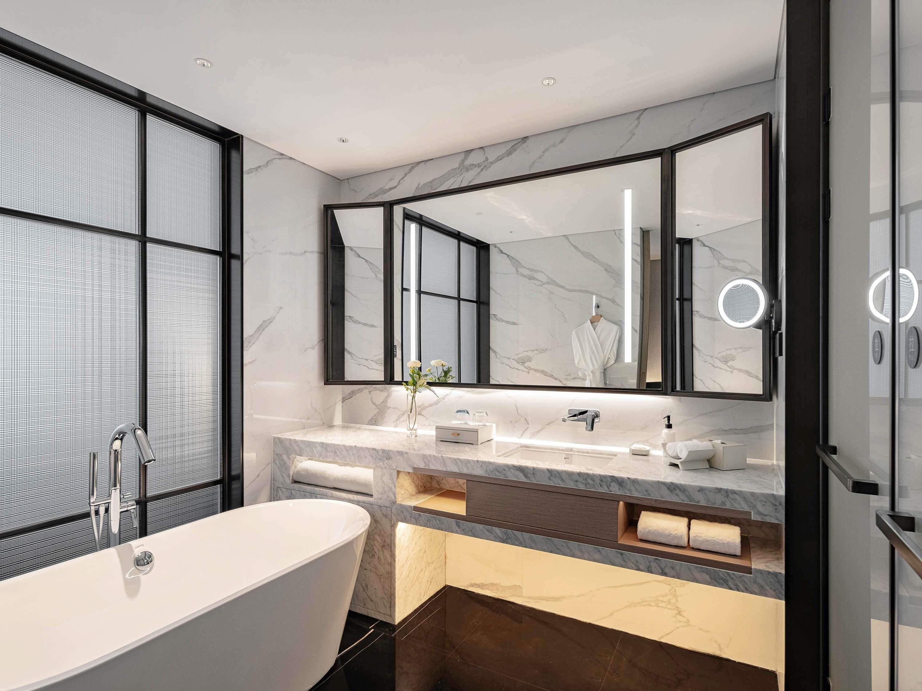 Un baño moderno con una bañera independiente, un espejo grande y un tocador con encimera de mármol.