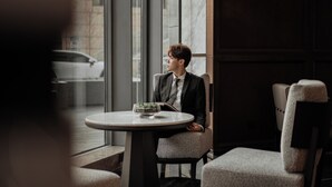 A man in a suit sitting at a round table with a small plant, in a room with large windows and a view of a car outside. - Grand Mercure Shenzhen Guangming (Shenzhen)