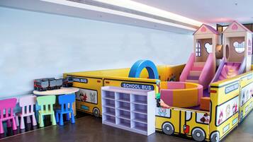 Uma área de recreação infantil com tema de ônibus escolar, incluindo uma casinha de brincar e cadeiras coloridas.