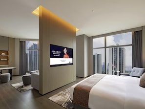 Habitación de hotel moderna con una cama grande, un televisor de pantalla plana montado en un panel de madera, un escritorio y vistas de edificios altos.