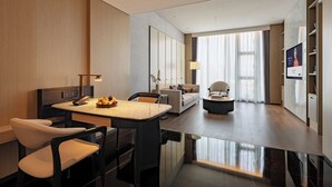 A modern hotel room with a dining area, a sofa, a TV, and a large window with curtains. - Grand Mercure Shenzhen Guangming (Shenzhen)