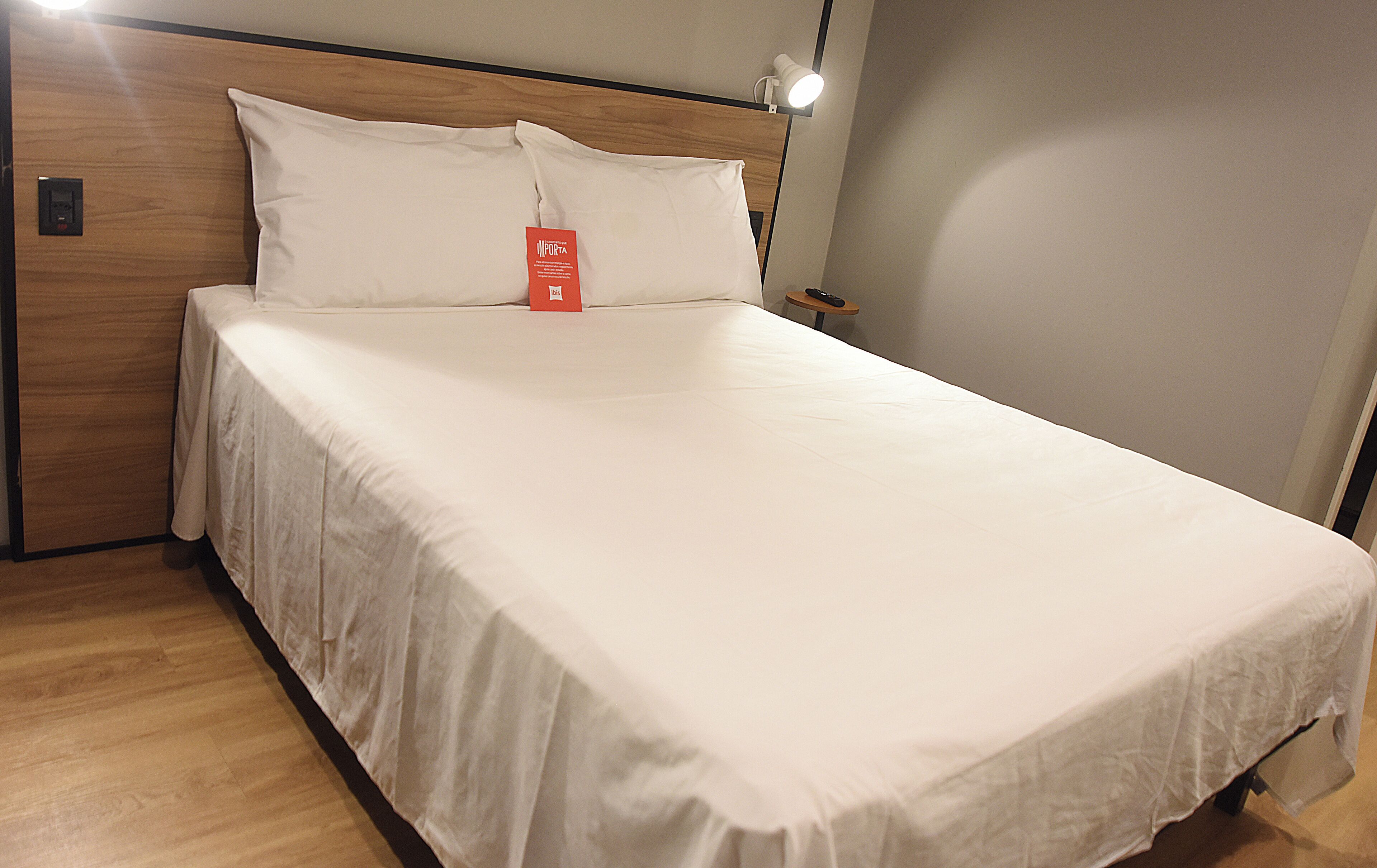 A neatly made bed with white linens, a wooden headboard, and a small bedside table with a lamp.