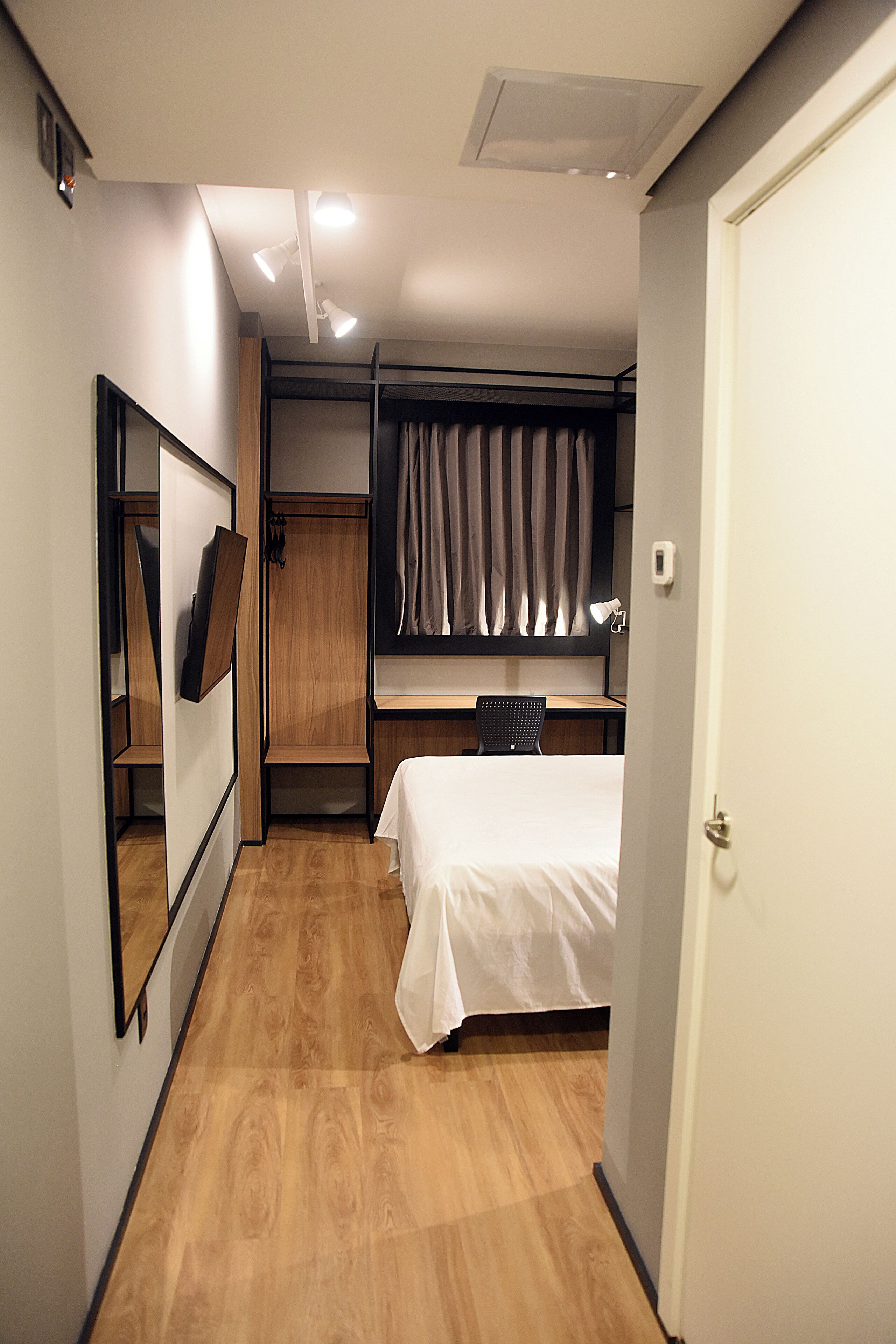 A compact hotel room with a bed, a desk, and a wardrobe.