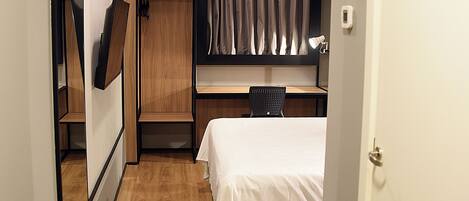A compact hotel room with a bed, a desk, and a wardrobe.