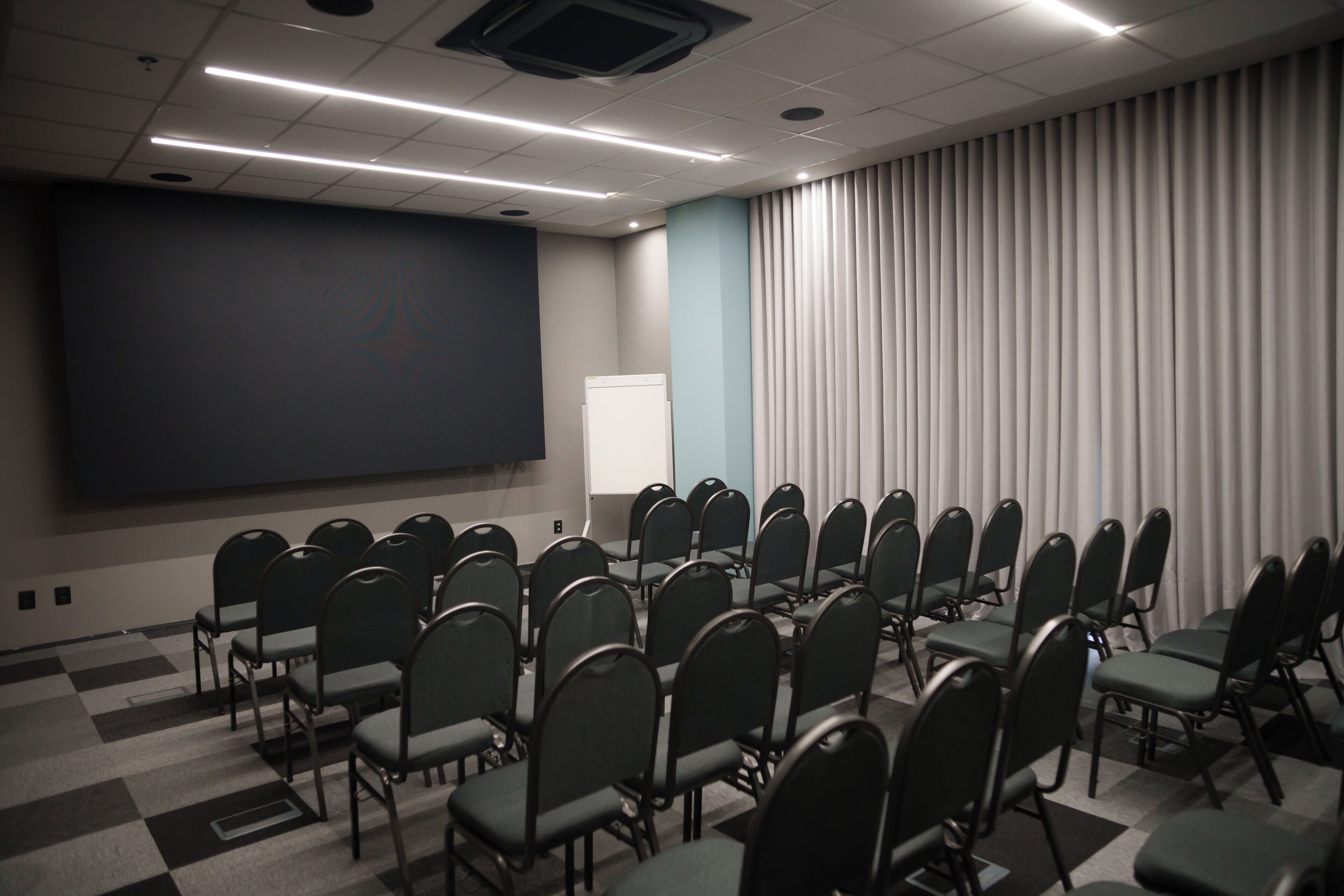 A conference room with rows of chairs, a projector screen, and a whiteboard.