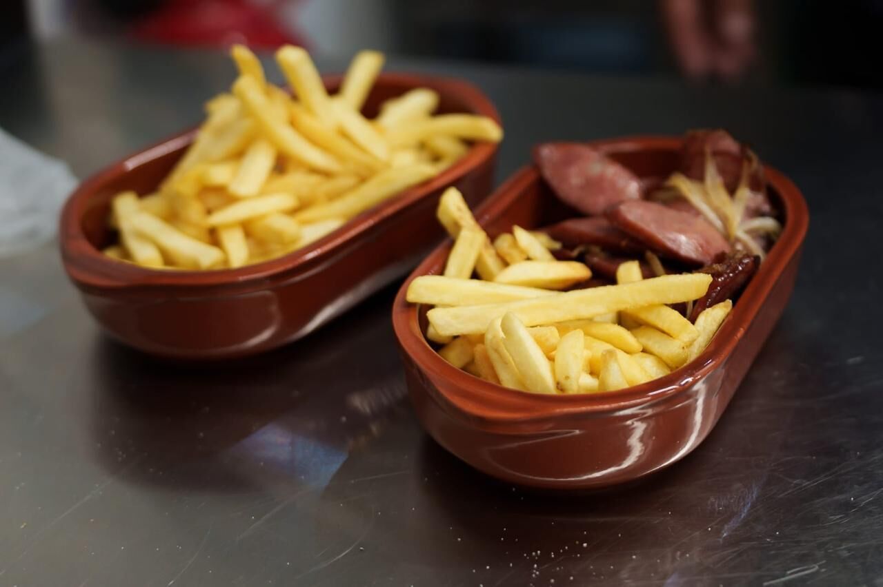 Two ceramic bowls filled with French fries and sausages.