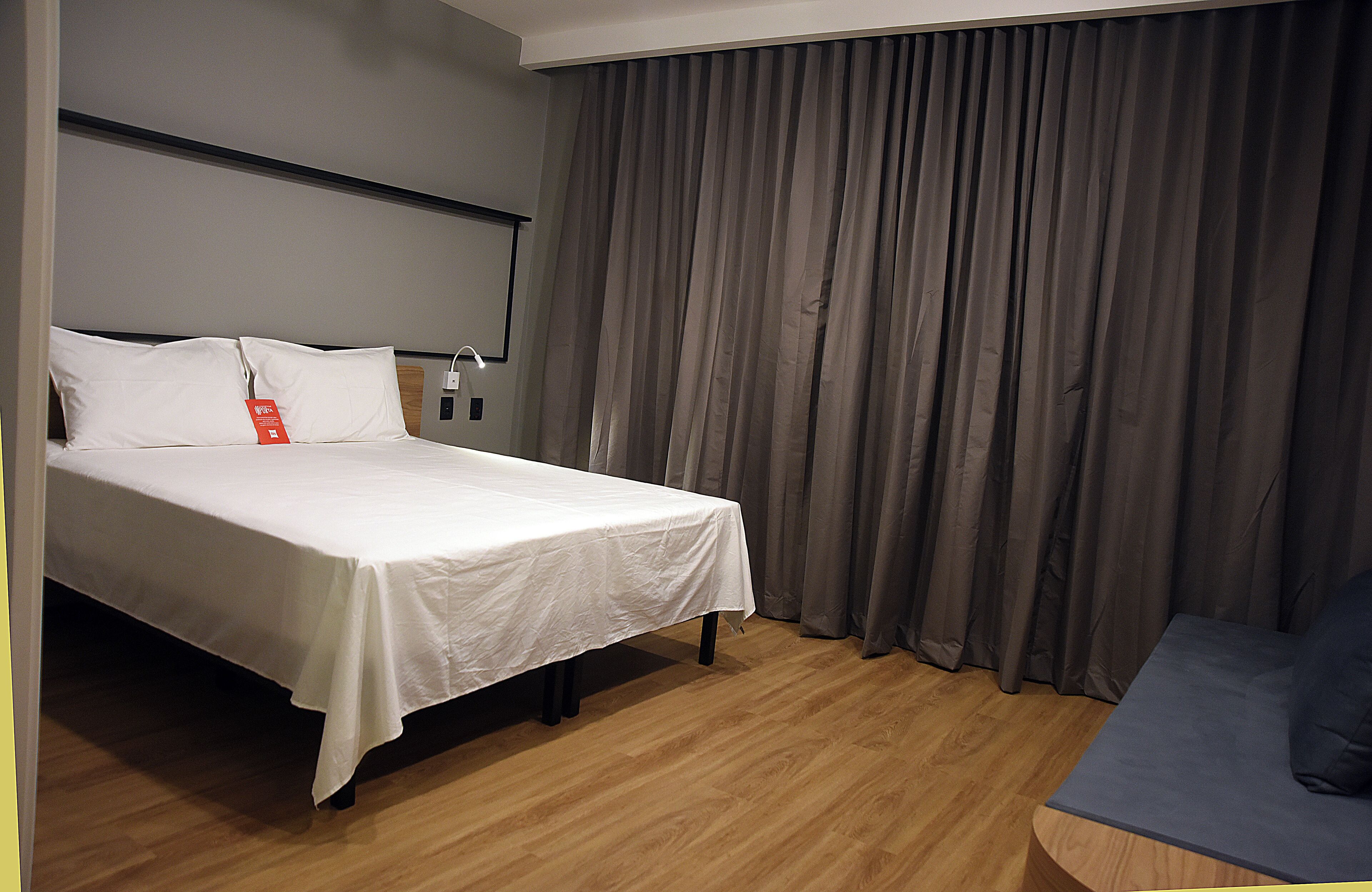 Een hotelkamer met een bed, nachtkastje, lamp en gordijn.